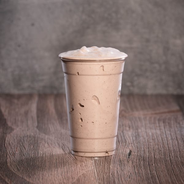 A Jerusalem Cafe kosher milkshake in a clear plastic cup sits on a wooden table.
