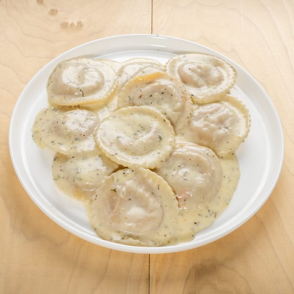 A white plate filled with kosher ravioli in a creamy sauce, garnished with herbs.