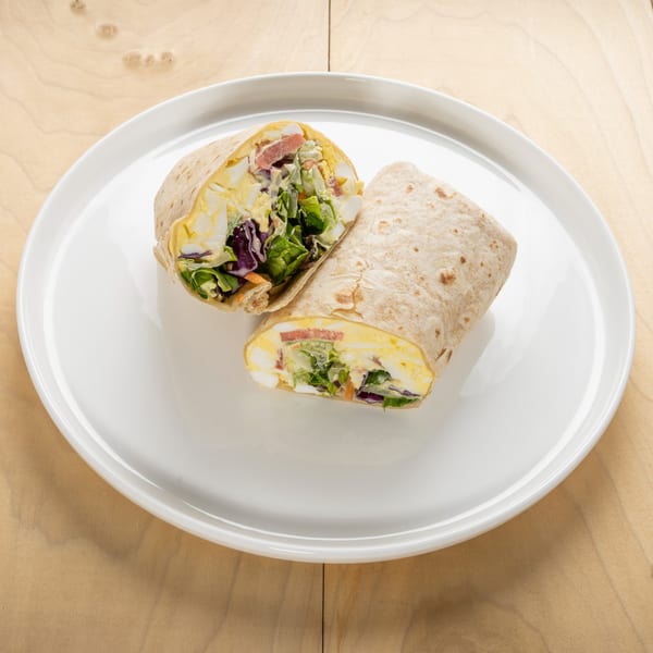 Two halves of a kosher egg salad wrap with lettuce, cabbage, and tomato on a white plate.