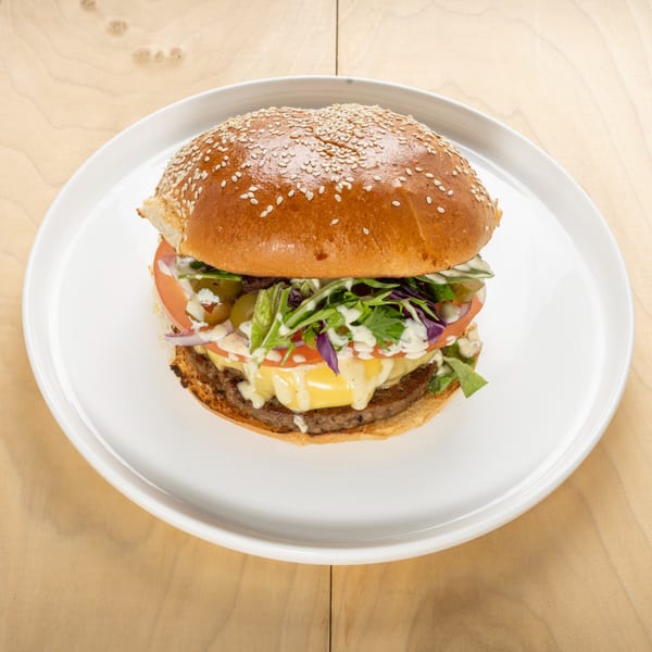 A kosher burger with melted cheese, lettuce, tomatoes, onions, and pickles on a sesame bun.