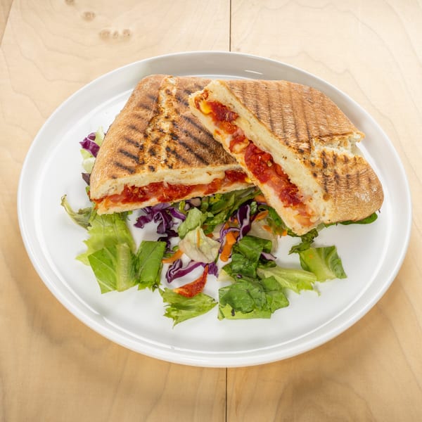 A grilled panini, cut in half, revealing melted cheese and red sauce, served with a side salad.