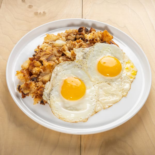 Two fried eggs with bright yellow yolks on a bed of crispy hash browns on a white plate.