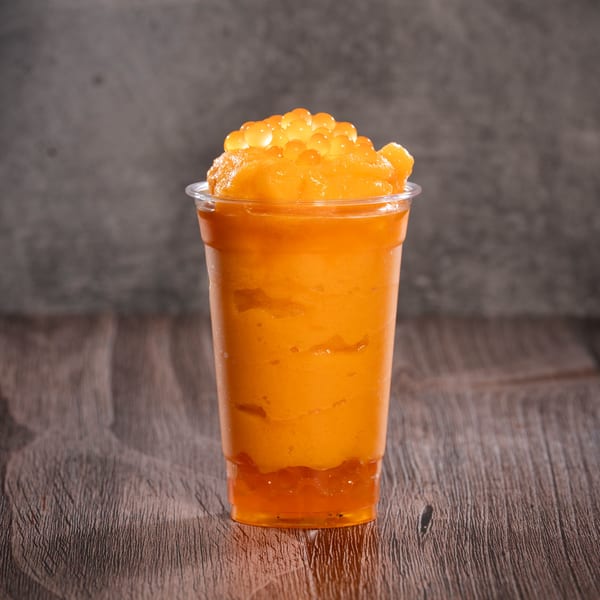 A vibrant orange slushy drink in a clear plastic cup, topped with orange boba pearls.