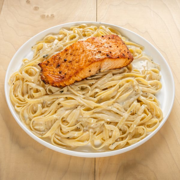 Kosher salmon fillet with creamy fettuccine pasta, served on a white plate.