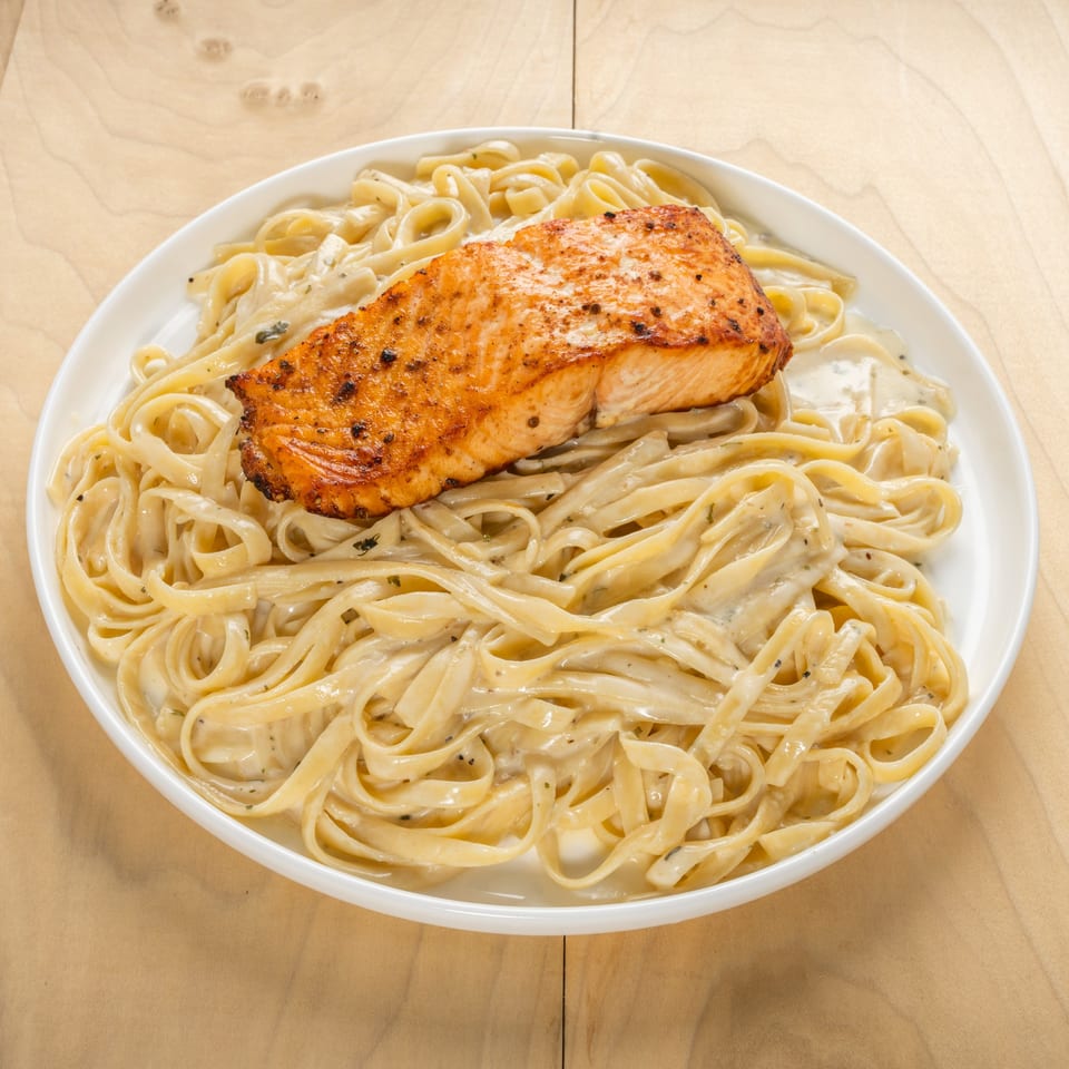 Kosher salmon fillet with creamy fettuccine pasta, served on a white plate.