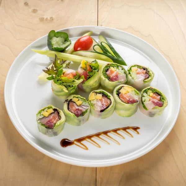 Kosher sushi rolls with fish, mango, and vegetables, garnished with celery, tomato, and cucumber.