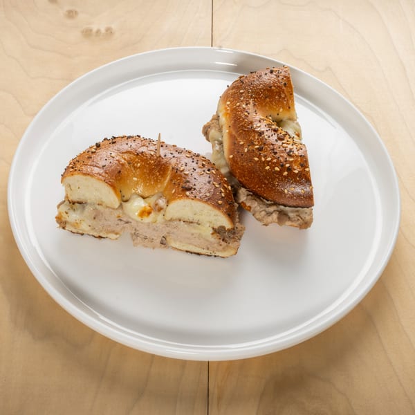 Two halves of an everything bagel sandwich with melted cheese and meat on a white plate.