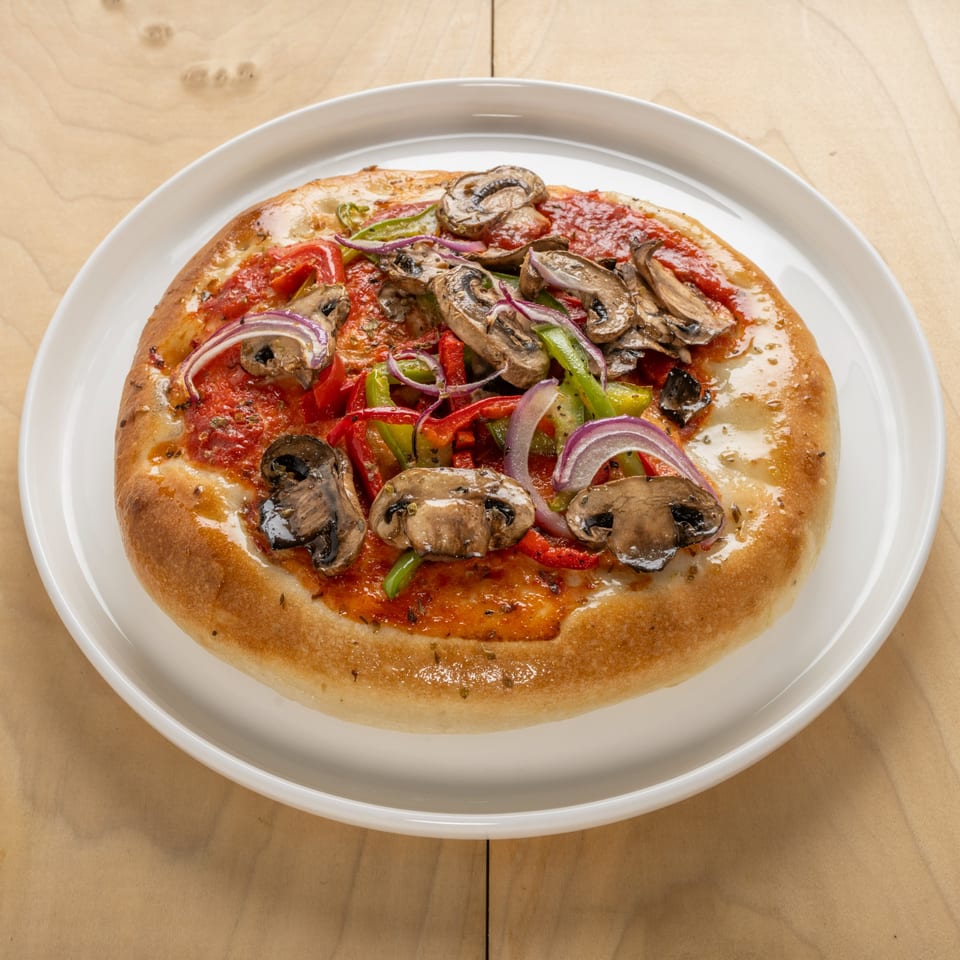 A Jerusalem Cafe kosher pizza with mushrooms, red and green peppers, and red onions on a white plate.