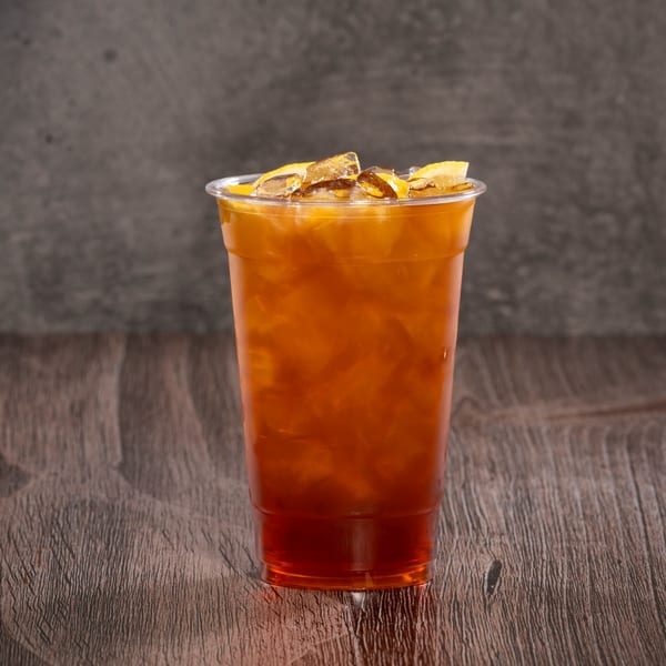 Iced tea with lemon slices and ice in a clear plastic cup on a wooden table.