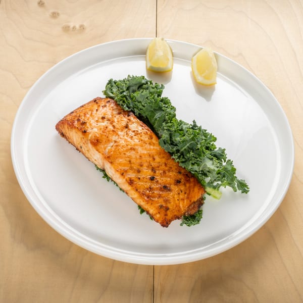 Kosher grilled salmon fillet with kale and lemon wedges on a white plate.