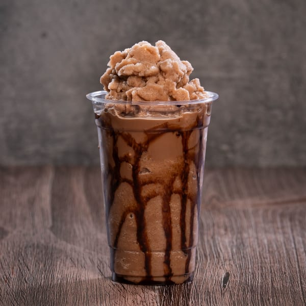 A chocolate milkshake with chocolate syrup drizzled inside the cup, topped with a scoop of frozen chocolate.