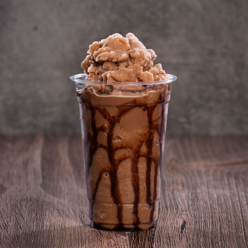 A chocolate milkshake with chocolate syrup drizzled inside the cup, topped with a scoop of frozen chocolate.